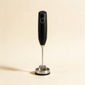 Black handheld milk frother standing in its counter stand