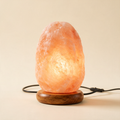 The Glow Himalayan pink salt lamp glowing amber on a wooden base