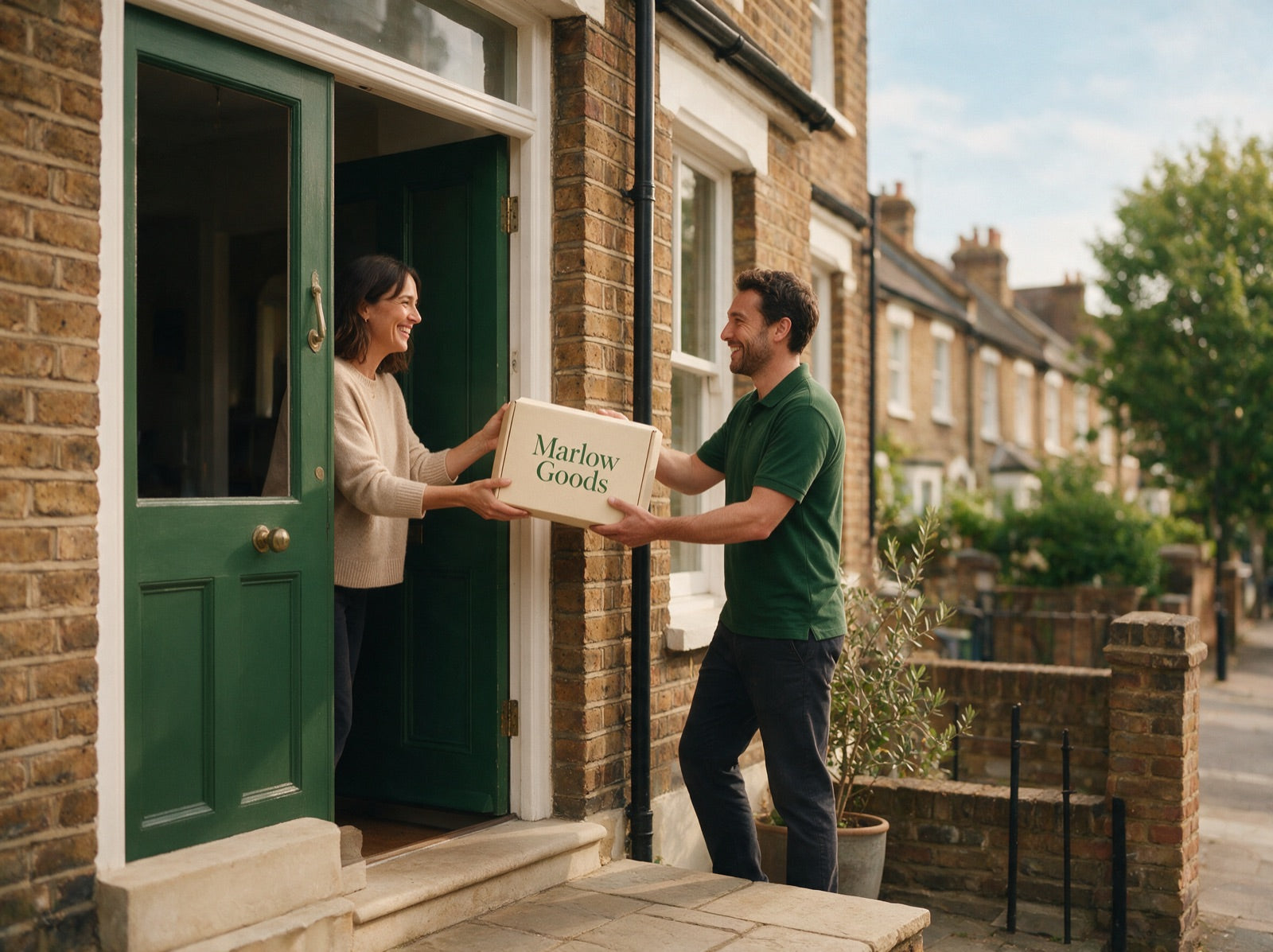 A courier hands a Marlow Goods parcel to a smiling customer at their front door
